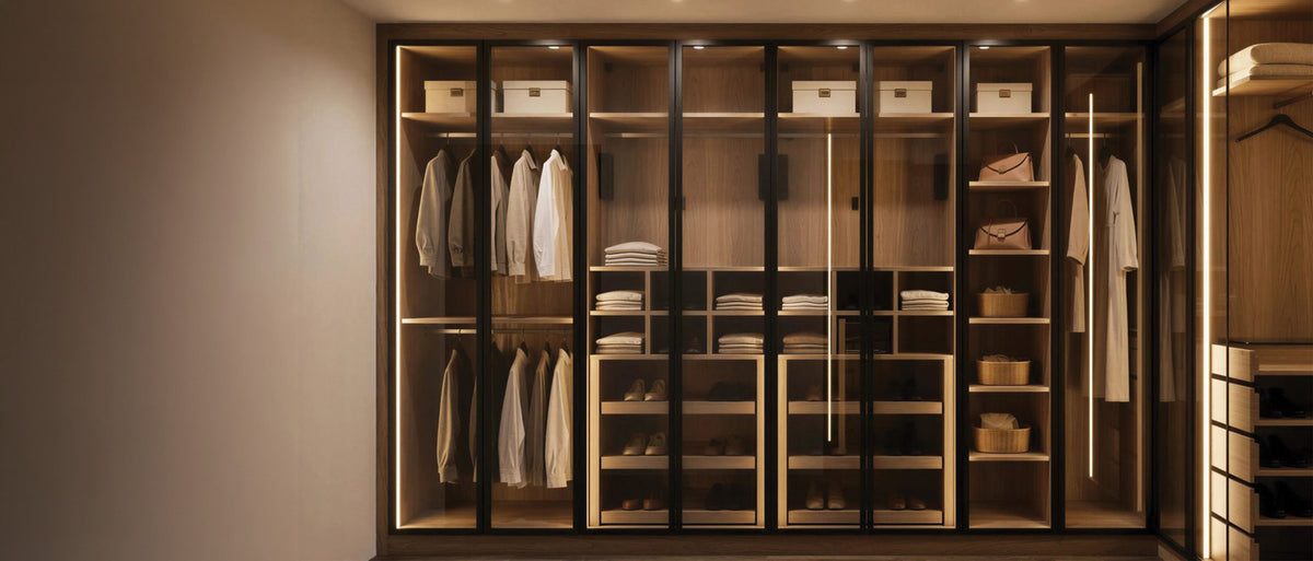 Glass-fronted fitted wardrobe wall with a lit walnut interior of hanging, shelves and drawers, made to measure in London