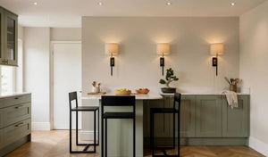 Hampstead sage green shaker kitchen: breakfast peninsula with a white worktop and two black stools under wall lights, London