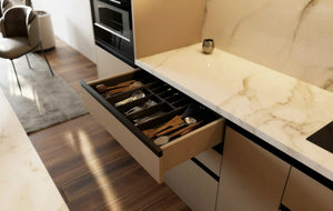 Maida Vale Handleless Kitchen in London: cream matt handleless doors with a white marble worktop, peninsula breakfast bar, walnut accents and black pendant lights; an open cutlery drawer under the white marble worktop. Made to measure by Metro Home Interiors