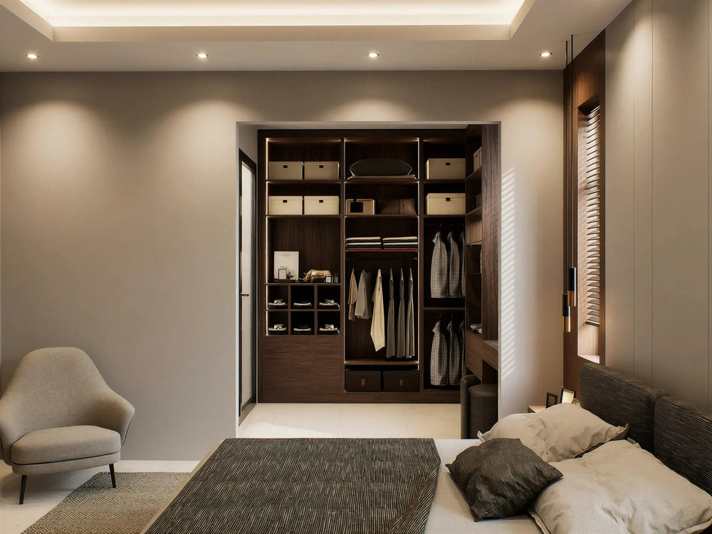 Pelham walk-in wardrobe in London seen from the bed: a walnut open dressing nook in the alcove with box shelves, lit hanging, shoe cubbies and drawers, and an armchair beside it. Made to measure by Metro Home Interiors