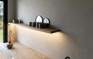 Shoreditch Oak Handleless Kitchen in London: light oak woodgrain handleless doors with a dark grey stone worktop, black tall units and a walnut dining table; a lit floating oak shelf over the marble-effect worktop. Made to measure by Metro Home Interiors