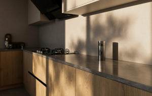 Shoreditch Oak Handleless Kitchen in London: light oak woodgrain handleless doors with a dark grey stone worktop, black tall units and a walnut dining table; the dark grey stone worktop and grip-rail base units along the main run. Made to measure by Metro Home Interiors