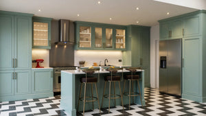 St John's Wood Shaker Island Kitchen in London: sage green in-frame shaker doors with brass handles, a white marble island with breakfast bar, a range cooker and a chevron tiled floor; the marble island, range cooker and glazed wall units. Made to measure by Metro Home Interiors