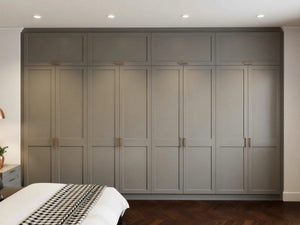 Vivienne fitted bedroom furniture in London: cream shaker wardrobe wall with slim black bar handles; the floor-to-ceiling cream shaker wardrobe wall from the bed. Made to measure by Metro Home Interiors