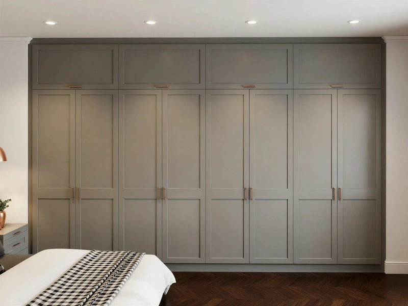 Vivienne fitted bedroom furniture in London: cream shaker wardrobe wall with slim black bar handles; the floor-to-ceiling cream shaker wardrobe wall from the bed. Made to measure by Metro Home Interiors