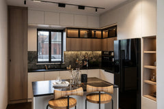 Blackheath Slab Island Kitchen in London: matt white slab base units with oak wall units, a black marble island and splashback, and a black fridge-freezer; the black marble island with timber stools under the window. Made to measure by Metro Home Interiors