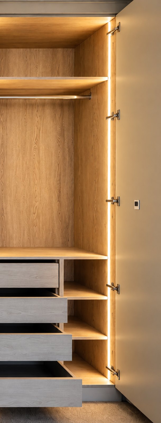 Warm LED strip lighting inside a fitted wardrobe with an oak interior, hanging rail, shelves and pull-out drawers