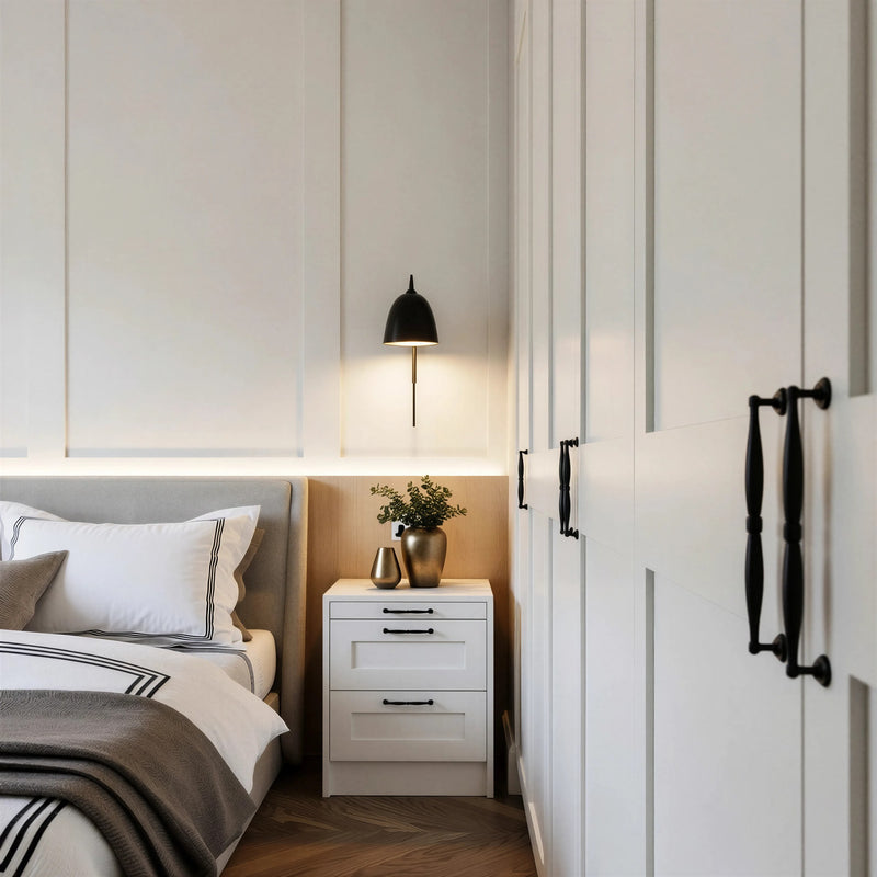 Hampstead shaker bedside: a white three-drawer shaker bedside with black handles beside the bed, under a wall light and panelled headboard wall