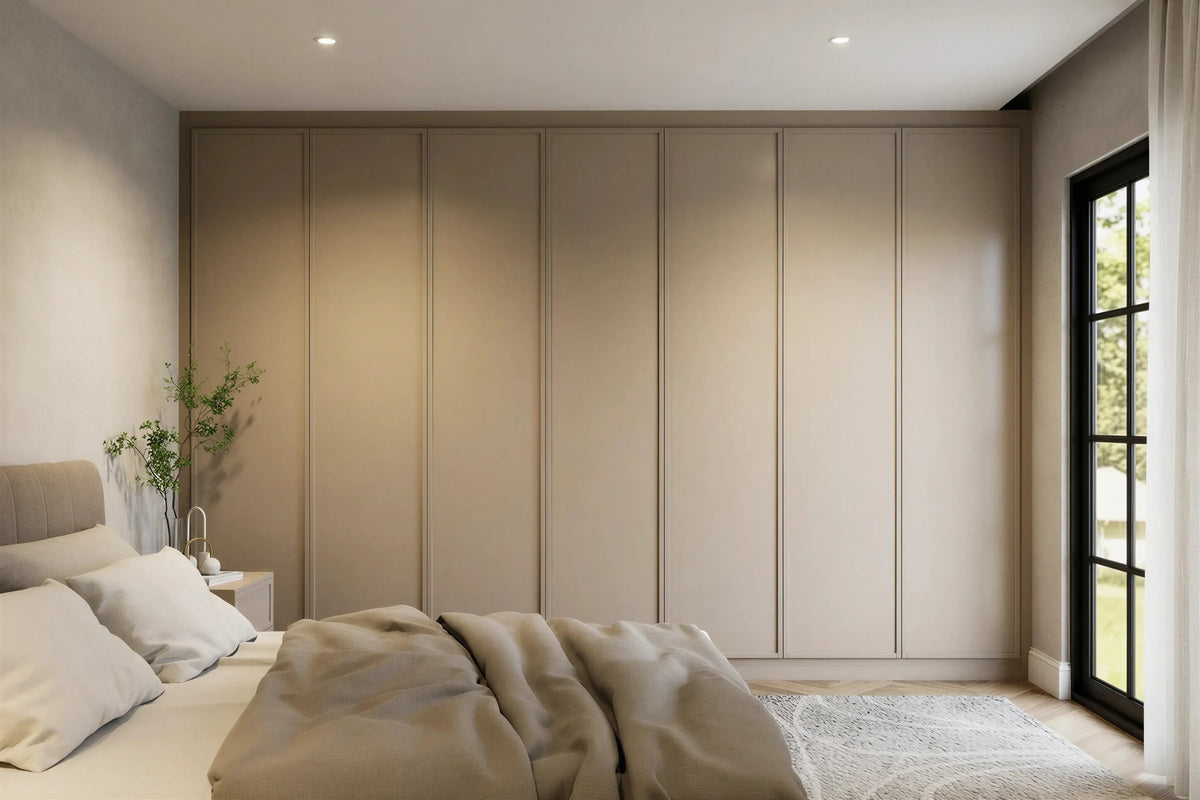 Imogen fitted bedroom furniture in London: cream panelled wardrobe wall wrapping the corner of the room; the cream panelled wardrobes wrapping the corner beside the window. Made to measure by Metro Home Interiors