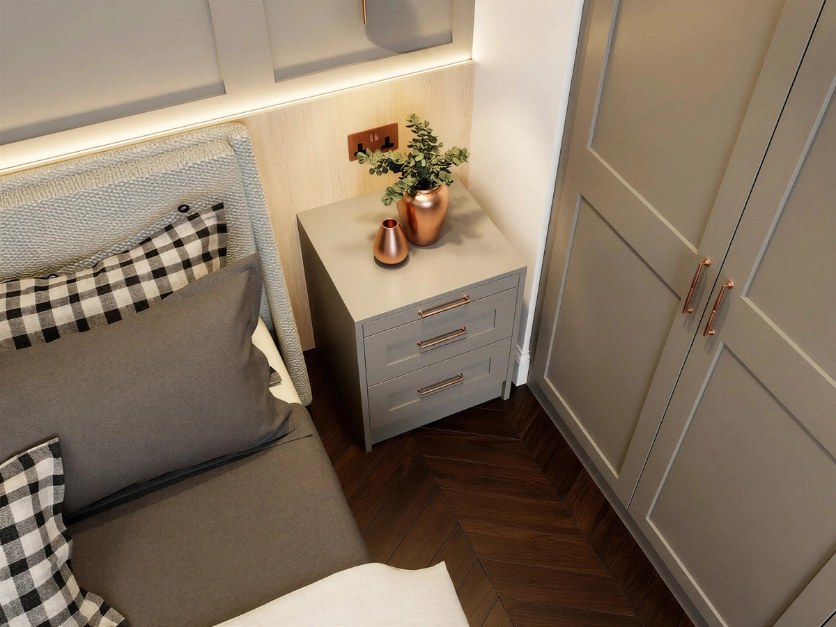 Kensal bedside: a grey three-drawer bedside with copper bar handles beside a grey upholstered bed, close up