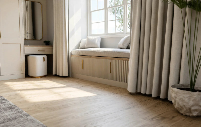 Seraphina fitted bedroom furniture in London: Cashmere Grey shaker wardrobes with brass bar handles; the built-in window seat with a lift-up lid beside the dressing table. Made to measure by Metro Home Interiors