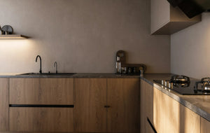 Shoreditch Oak Handleless Kitchen in London: light oak woodgrain handleless doors with a dark grey stone worktop, black tall units and a walnut dining table; the sink run with black tap under lit wall units. Made to measure by Metro Home Interiors