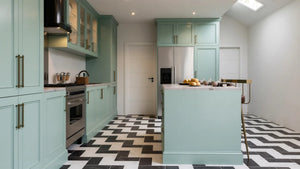 St John's Wood Shaker Island Kitchen in London: sage green in-frame shaker doors with brass handles, a white marble island with breakfast bar, a range cooker and a chevron tiled floor; the tall pantry run and island under a skylight. Made to measure by Metro Home Interiors