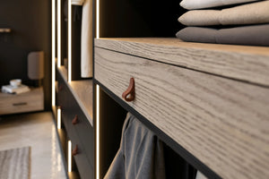 Thurloe walk-in wardrobe in London, close up: a pale ash drawer box with a stitched leather tab in the black carcass, folded knitwear above and an LED strip down the divider. Made to measure by Metro Home Interiors